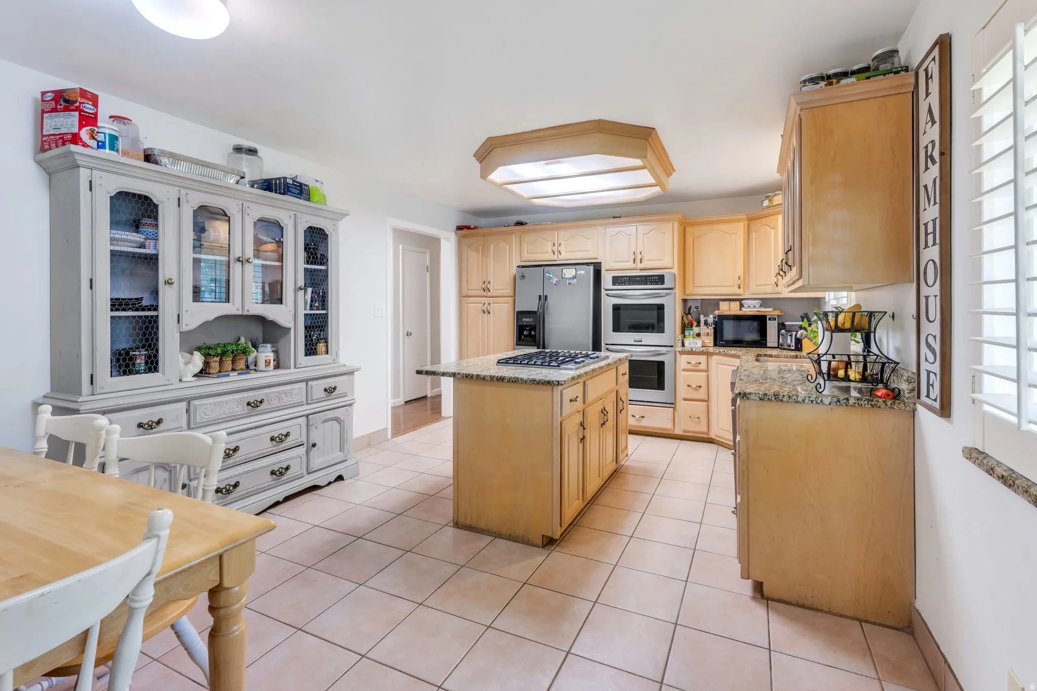 Spacious kitchen featuring natural wood cabinetry, stainless steel appliances, a gas cooktop, tile countertops, and a central island with seating