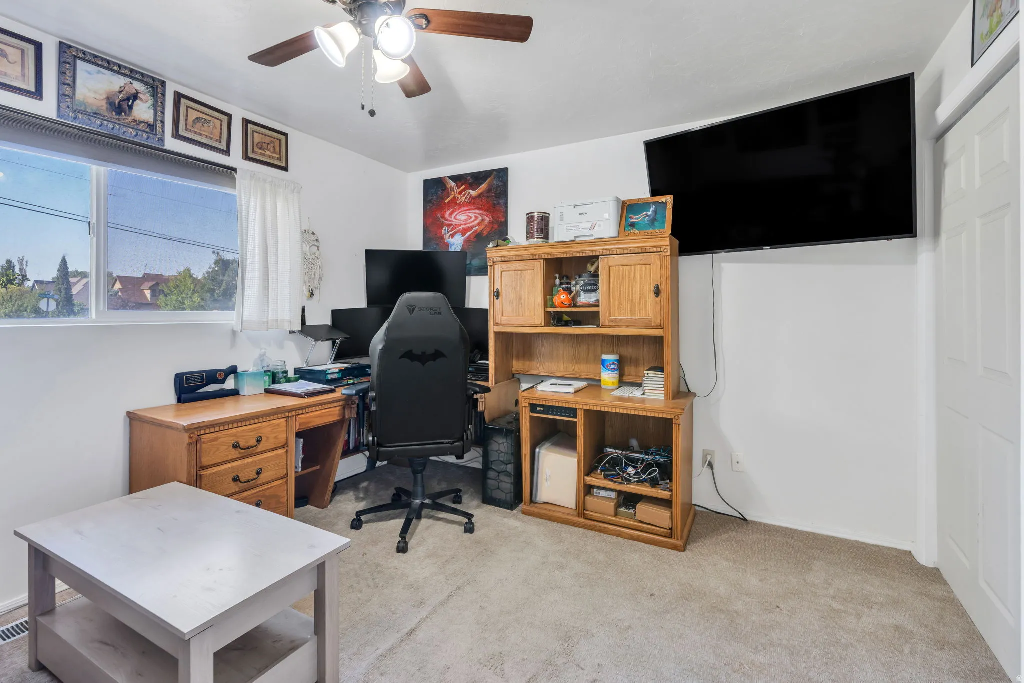 Versatile bonus room featuring carpeted flooring, abundant natural light from large windows, wooden cabinetry with open shelving, and a ceiling fan