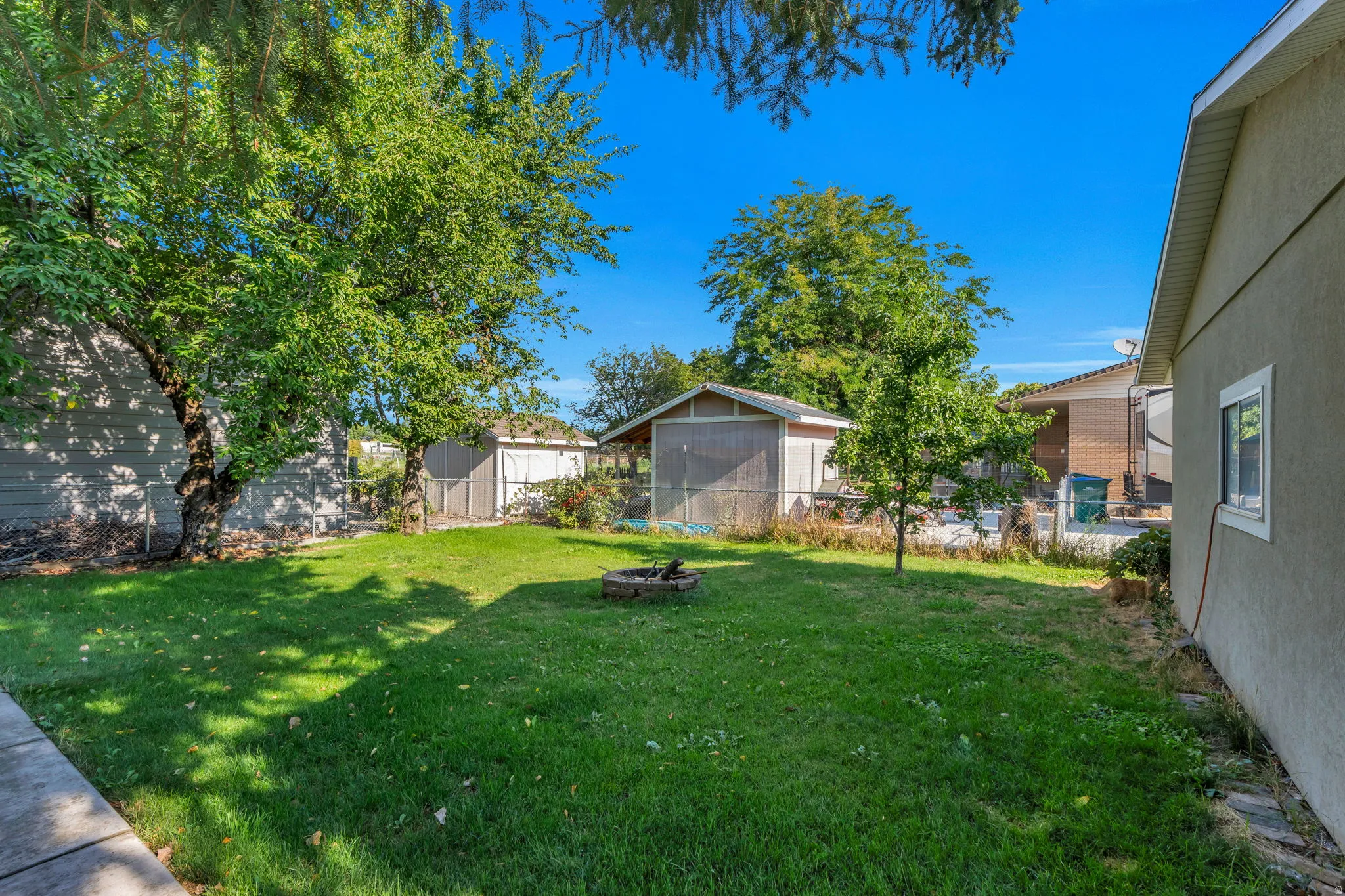 Expansive backyard featuring a mature tree canopy, lush manicured lawn, and multiple outbuildings