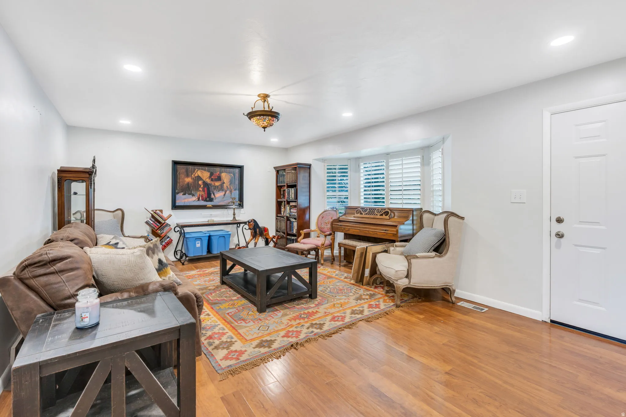Spacious living room showcasing hardwood flooring, recessed ceiling lighting, and a brass-finished pendant fixture