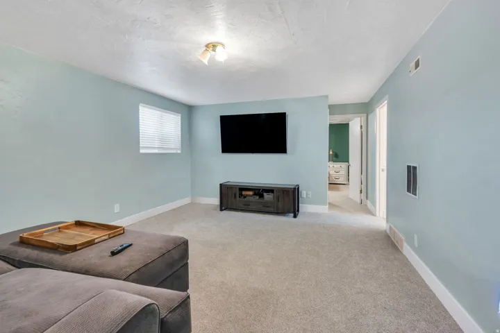 Spacious recreation room featuring light blue painted walls, neutral carpet flooring, a wall-mounted flat-screen television, and a built-in media console with storage