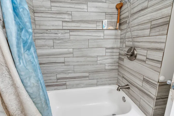 Updated bathroom featuring linear wood-finish tile surround, white soaking tub with chrome fixtures, and handheld showerhead