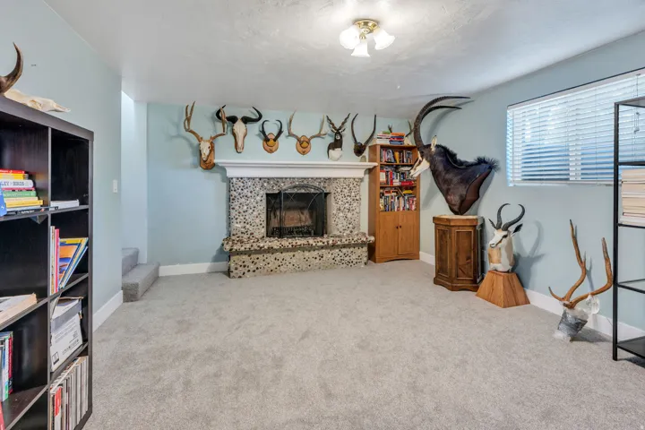 Spacious recreation room featuring a stone fireplace with wood mantel, carpeted flooring, recessed ceiling lighting, and built-in wooden cabinetry