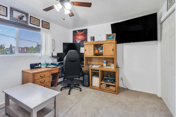 Versatile bonus room featuring carpeted flooring, abundant natural light from large windows, wooden cabinetry with open shelving, and a ceiling fan