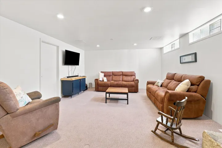 Spacious basement recreation room featuring recessed ceiling lighting, neutral carpeting, and multiple seating areas
