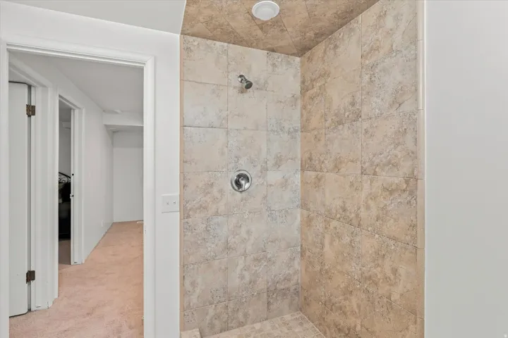 Spa-inspired shower enclosure featuring travertine tile walls, dual showerheads, and a frameless glass partition