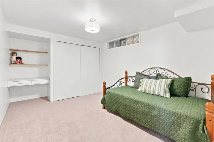 Spacious secondary bedroom with carpeted flooring, metal-frame bed with wood posts, built-in closet with sliding doors, and recessed ceiling lighting