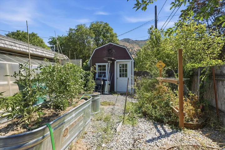 Charming backyard retreat featuring a detached shed with barn-style roof and dual French doors, surrounded by mature landscaping and raised garden beds