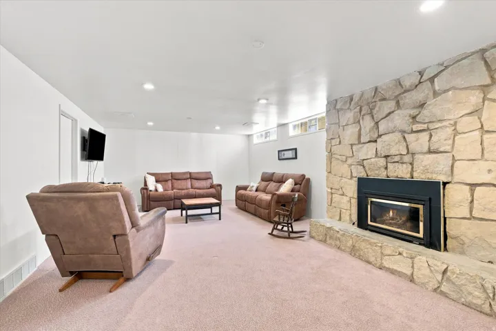Spacious recreation room featuring plush wall-to-wall carpeting, recessed ceiling lighting, and a striking stone fireplace with integrated gas insert