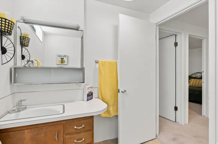 Bright bathroom featuring a curved vanity with wood-finish cabinetry and dual drawers, white countertop, and chrome fixtures