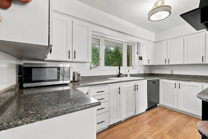 Kitchen featuring white cabinetry, dark speckled countertops, wood-finish flooring, a stainless steel dishwasher, and a window above the sink