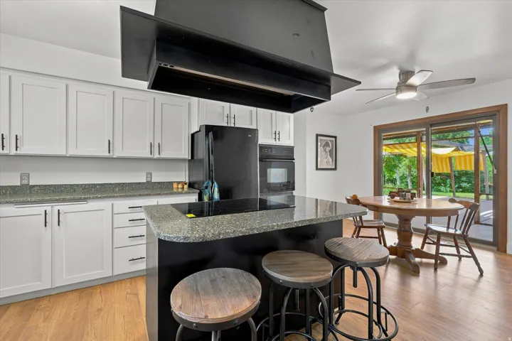 Kitchen featuring light-toned cabinetry with dark hardware, dark countertops, dark built-in appliances, and wood-finish flooring