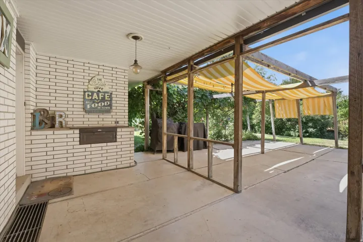 Covered patio featuring a built-in white brick outdoor kitchen, concrete flooring, and a wood-framed pergola with retractable awnings