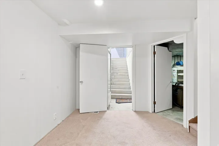 Bright, open basement space with neutral carpet flooring, recessed ceiling lighting, and direct staircase access