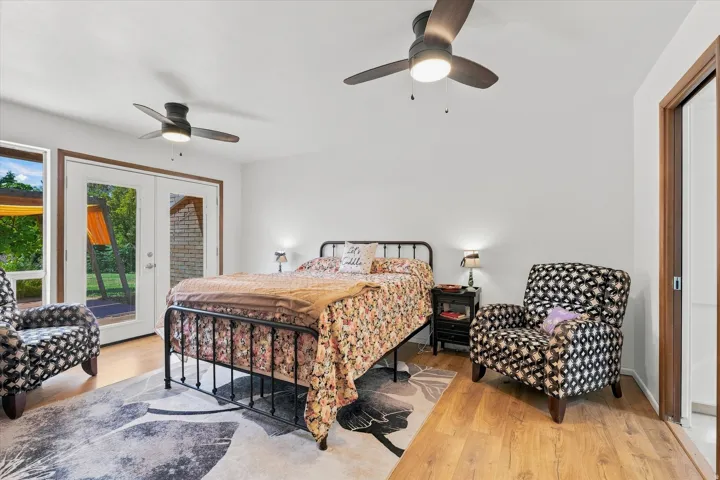 Spacious bedroom featuring hardwood flooring, ceiling fans with integrated lighting, and glass sliding doors opening to outdoor space