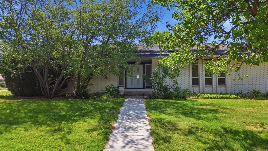 Brick residence with a manicured lawn and mature shade trees framing the front elevation