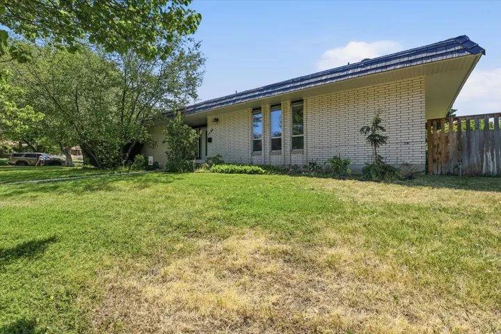 Brick exterior featuring a sloped roofline, multiple windows, and partial fencing