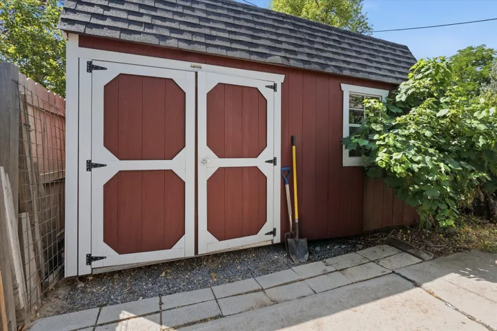 Red storage shed with white double doors, a gabled roof, and a single window