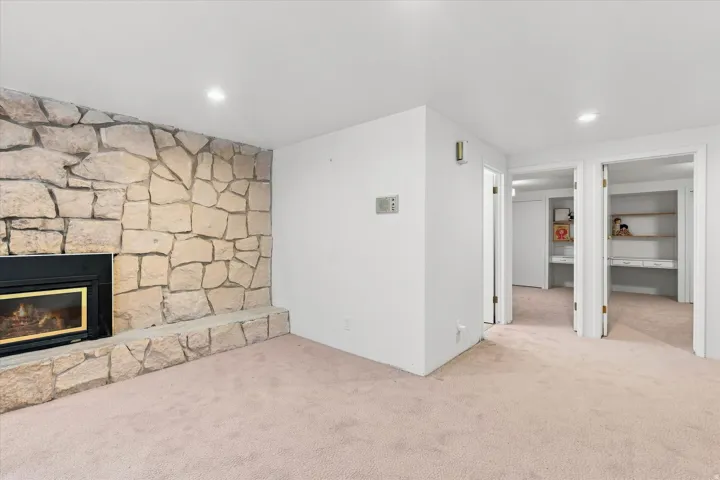Spacious lower-level recreation room featuring a stone fireplace with gas insert, neutral carpet flooring, and multiple closet storage
