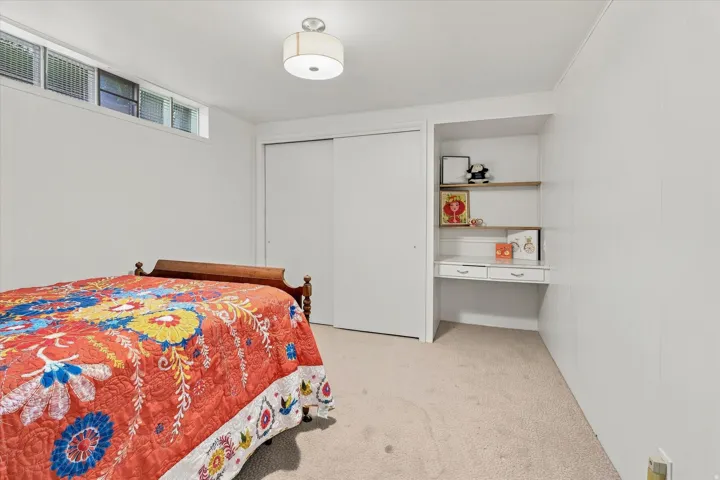 White walls, carpet flooring, a ceiling-mounted light fixture, sliding closet doors, and built-in shelving with a desk