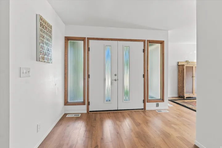 Bright entryway showcasing gleaming wood-finish flooring, white walls, and custom wood-framed glass closet doors with mirrored panels