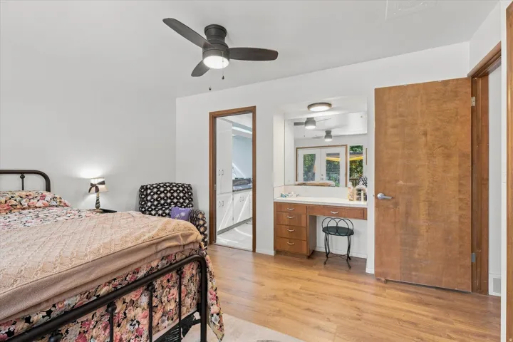 Wood-finish flooring, built-in vanity with mirror, built-in drawer storage, and ceiling fan with integrated lighting