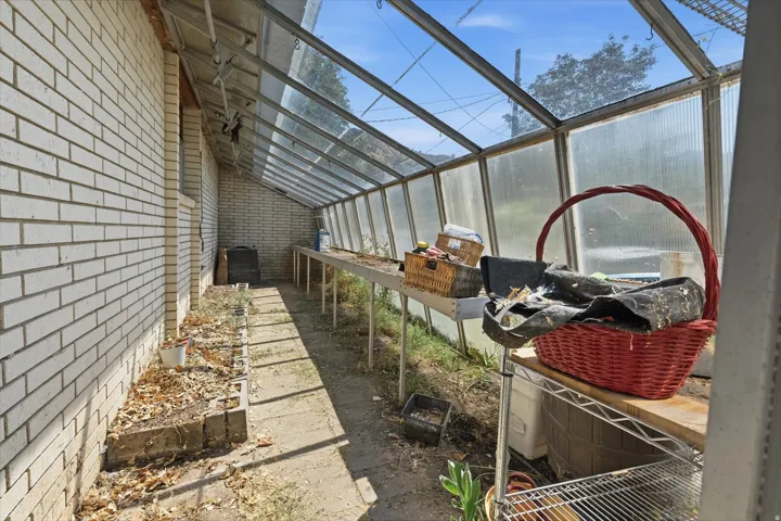 Greenhouse structure featuring a clear panel roof and side walls, a brick exterior wall, and built-in shelving