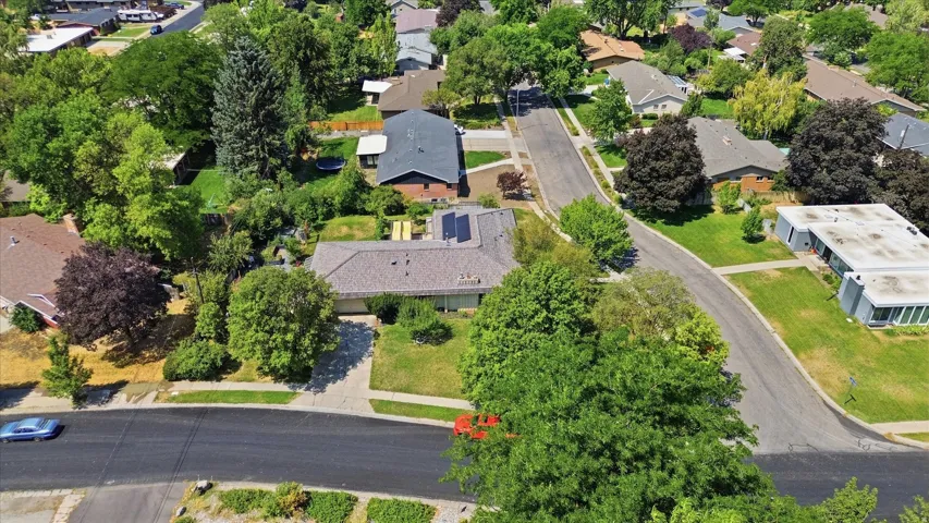 Charming residence situated on a tree-lined street, featuring a dark-shingled roof, manicured lawn, and mature landscaping throughout the property