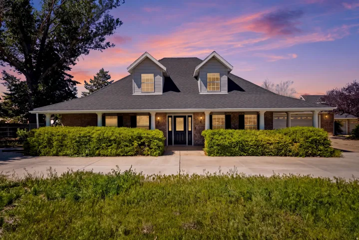 Brick facade with gray siding accents, dark roof, dormer windows, and a covered front porch with white columns