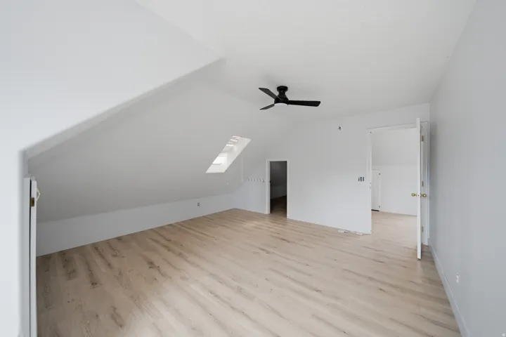 Spacious attic bedroom with peaked vaulted ceilings, abundant natural light from skylights, wood-finish flooring throughout, and ceiling fan
