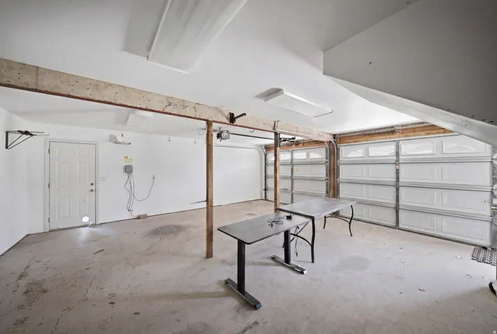 Concrete flooring, white interior walls, overhead fluorescent lighting, two garage doors, and a paneled interior door