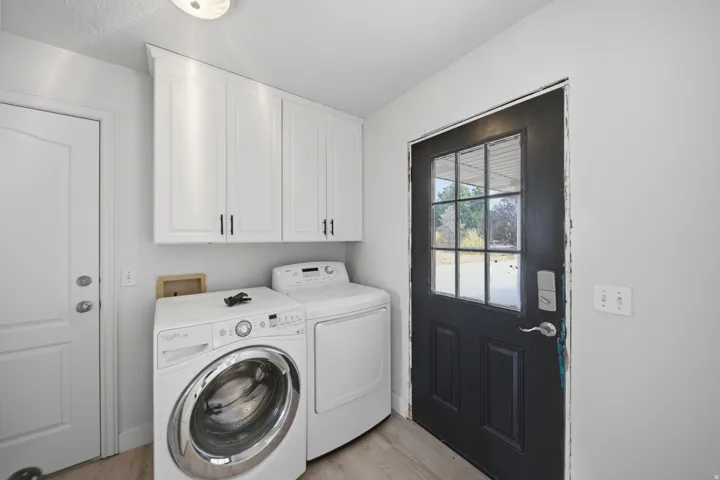Light wood-finish flooring, white wall-mounted cabinetry with matte black hardware, and a black exterior door with window panes