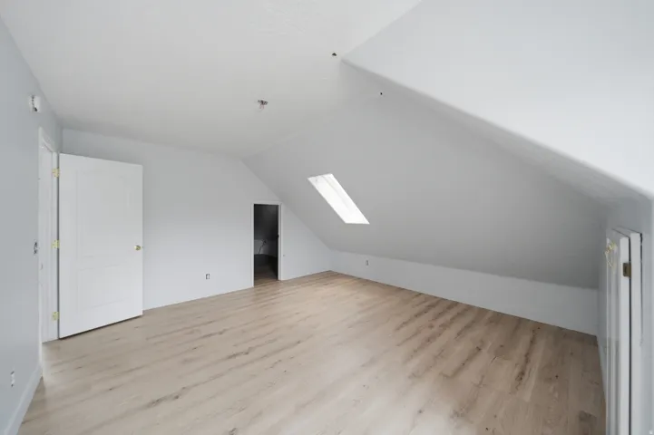 Bright attic space with sloped ceilings, skylights providing natural illumination, light wood-finish flooring throughout, and multiple closet storage areas