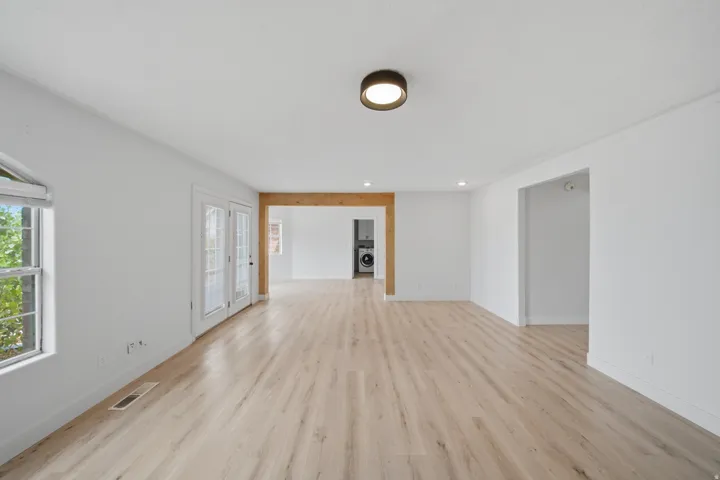 Light wood-finish flooring, white walls, double French doors, wood-beam archway, and recessed lighting