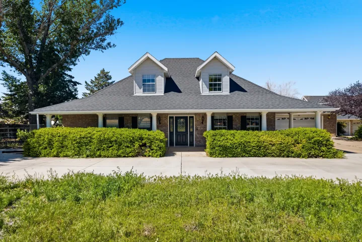 Charming Colonial-style residence featuring a symmetrical facade with dual peaked dormers, black shutters, and a covered front porch