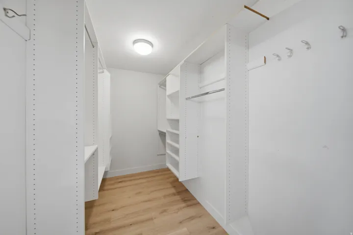 Customizable built-in shelving, hanging rods, light wood-finish flooring, and flush-mount lighting