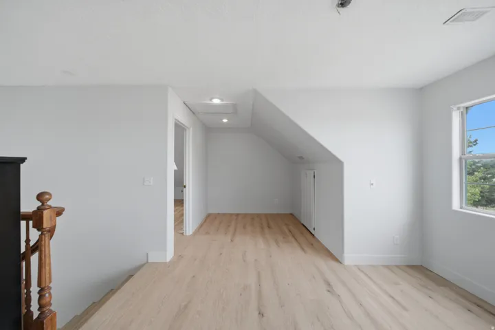 Bright upper-level hallway featuring wide-plank wood-finish flooring, fresh white walls, recessed ceiling lighting, and abundant natural light from a large window