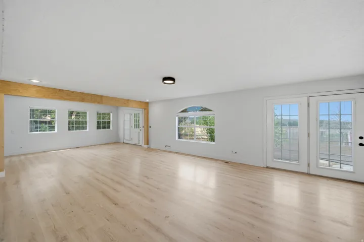Expansive room featuring light wood-finish flooring, multiple windows, a decorative arched window, and double French doors