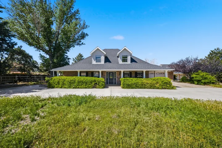 Dormer windows, covered front porch, brick facade, attached garage, and mature landscaping