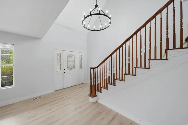 Bright foyer showcasing a striking open staircase with dark wood railings and balusters, light wood-finish flooring, and abundant natural light from a multi-pane window