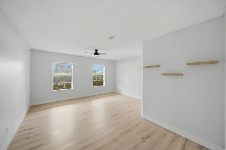 Spacious room featuring light wood-finish flooring, multiple windows, a ceiling fan, and built-in wall shelving