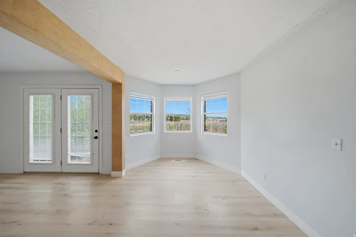 Light wood-finish flooring, white double French doors, large bay windows, and a prominent wood ceiling beam