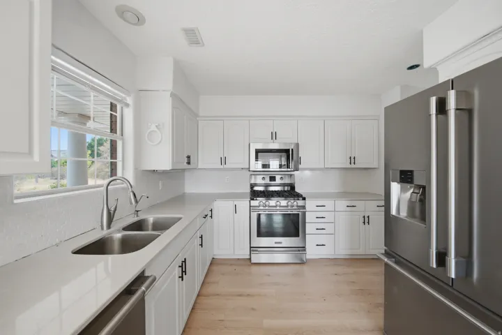 White cabinetry, stainless steel appliances, wood-finish flooring, undermount double-basin sink, and light-toned countertops