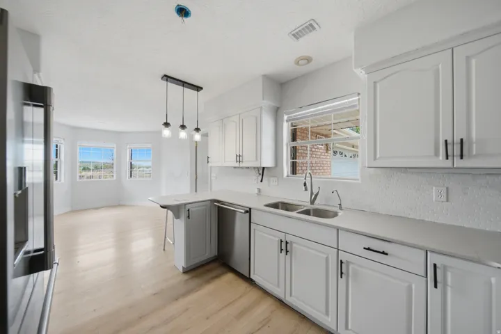 Modern kitchen featuring white cabinetry with black hardware, stainless steel appliances including a French-door refrigerator, quartz countertops, subway tile backsplash, and pendant lighting above the island