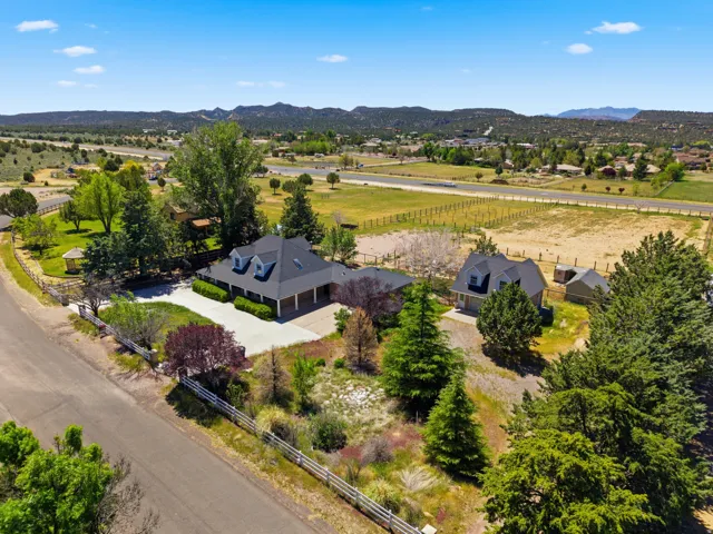 Property featuring two structures, paved driveways, a white picket fence, mature trees, and mountainous terrain