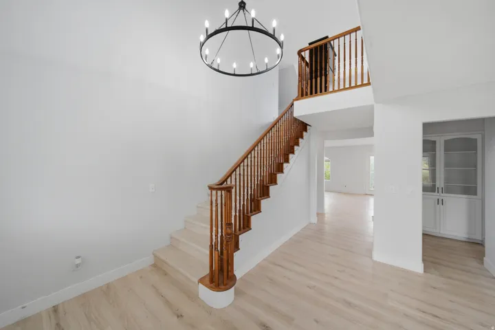 Two-story entry featuring light wood-finish flooring, a grand staircase with wood banister, a second-story landing, a large iron chandelier, and built-in white cabinetry with glass doors