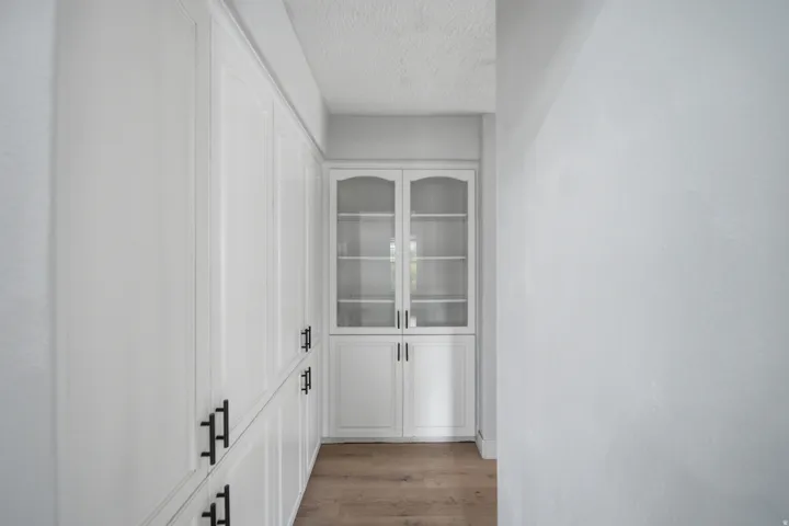 Bright hallway corridor showcasing custom cabinetry with glass-front upper doors and solid lower panels, accented by matte black hardware