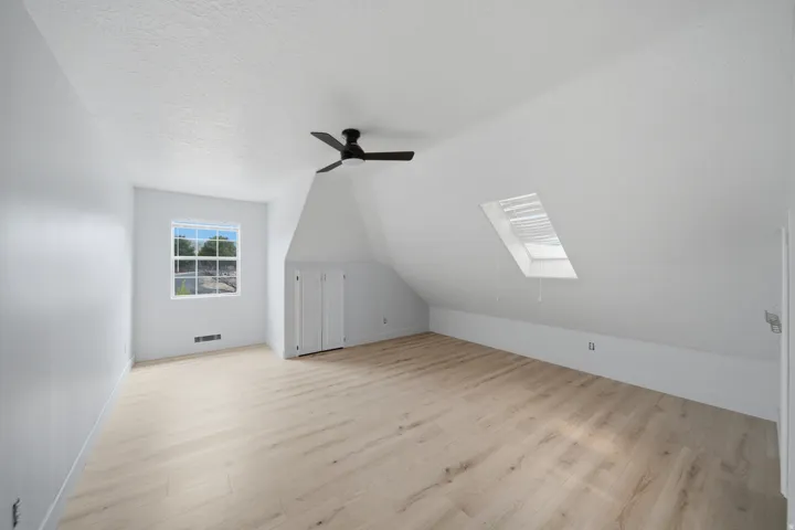 Light wood-finish flooring with a ceiling fan, a window, a skylight, and built-in white cabinetry