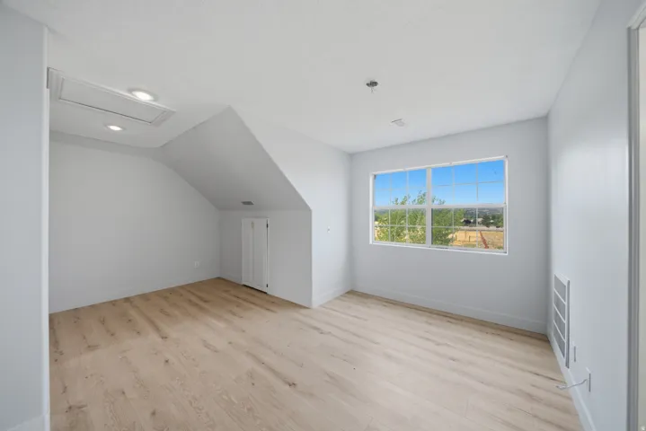 Bright upper-level bedroom featuring sloped vaulted ceilings, wood-finish flooring, and a large window framing natural light and outdoor scenery