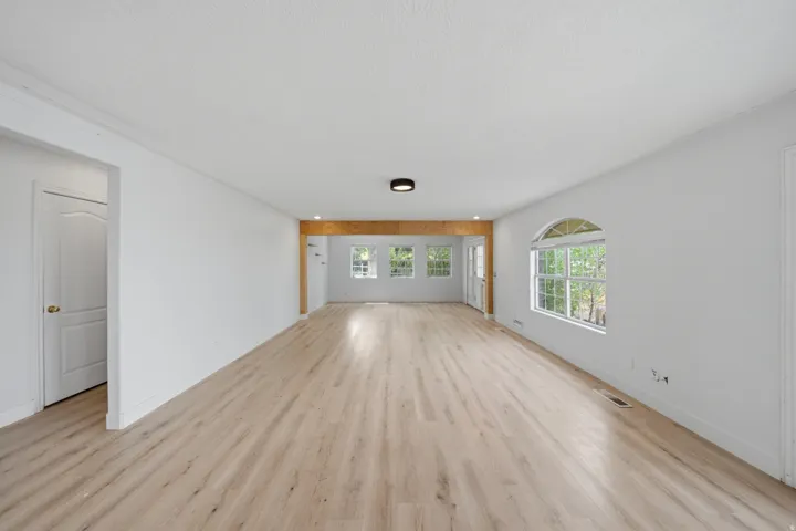Spacious room featuring wood-finish flooring, white walls, and an arched window